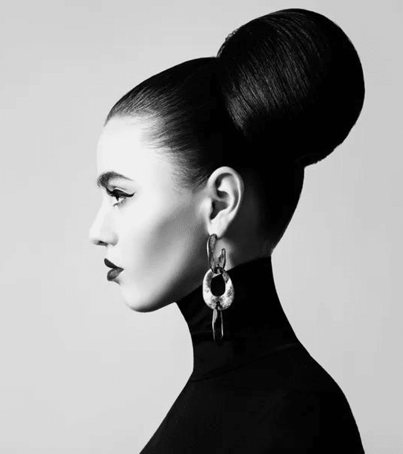 Profile of a woman with an elegant updo and bold earrings, dressed in a black turtleneck.